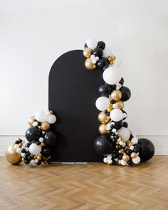 black and white balloons are arranged in the shape of an arch on a wooden floor