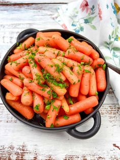 carrots with parsley in a black bowl on a white tablecloth next to a spoon