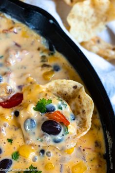 a tortilla chip being dipped with cheese and black olives in a skillet