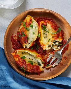 a wooden bowl filled with stuffed shells covered in marinara sauce and parmesan cheese