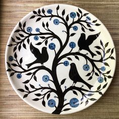 a white plate with blue flowers and birds painted on the side, sitting on a wooden table