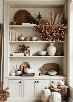 the shelves are filled with white dishes and pumpkins