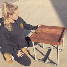 a woman sitting on the ground next to a wooden table with one leg bent over it