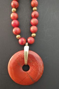 a red beaded necklace on a black surface with a gold plated pendant hanging from it