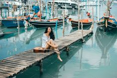 a woman sitting on a dock with boats in the background