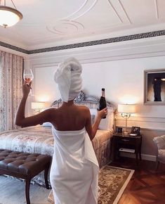 a woman in a bathrobe holding a glass of wine and looking at the bed