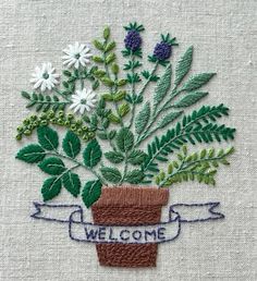 a potted plant with flowers is embroidered onto a piece of fabric that says welcome