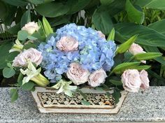 blue and pink flowers are in a vase on a stone ledge next to green leaves