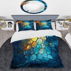 a bed with a blue and yellow comforter next to a mirror on the wall