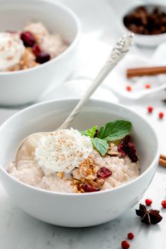 two white bowls filled with oatmeal topped with whipped cream and cranberries