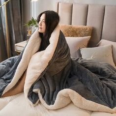 a woman laying on top of a bed covered in a gray and white blanket next to a lamp