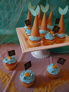 cupcakes with blue frosting and orange cones on a tray next to other cupcakes