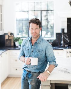 a man standing in a kitchen holding a coffee cup and looking at the camera while smiling