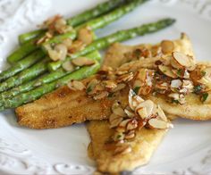 a white plate topped with chicken and asparagus covered in almonds on top of it