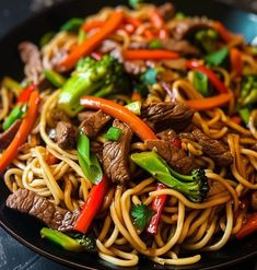 a black plate topped with beef and noodles covered in broccoli, peppers and carrots