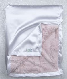 a pink and white blanket laying on top of a bed covered in a satin material