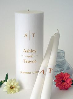 two white candles sitting on top of a table next to a vase with flowers in it