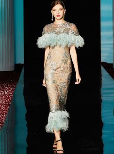 a woman walking down a runway wearing a dress with feathers on the top and bottom