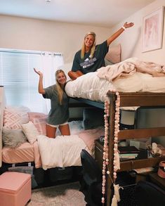 two women standing on top of a bunk bed in a room with lots of clutter