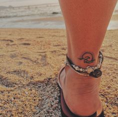 a woman's foot with a tattoo on the sand at the beach by the ocean