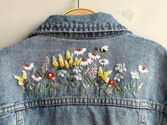 an embroidered denim jacket with daisies and bees on the back, hanging from a wall