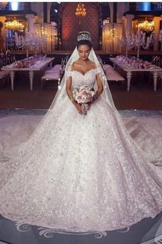 a woman in a wedding dress standing on a floor with tables and chandeliers