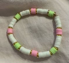 a white bracelet with pink, green and gold beads on top of a white cloth