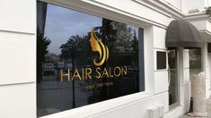 a hair salon sign on the side of a white building next to a sidewalk and trees