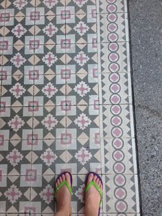 a woman's feet with green and blue sandals standing in front of a tiled floor