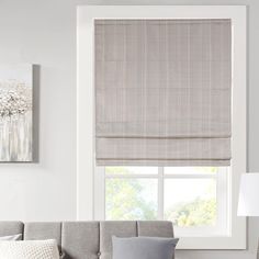 a living room with a gray couch and two windows covered in roman blind shades on the window sill