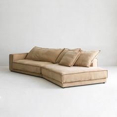 a large sectional couch with pillows on it in a white living room area that is lit by a window