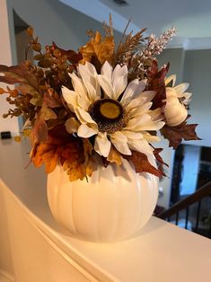 a white vase filled with lots of flowers on top of a counter next to a stair case