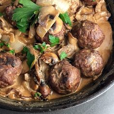 some meatballs and mushrooms are in a brown gravy with parsley on top