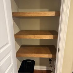 an empty closet with some shelves and a trash can on the floor next to it