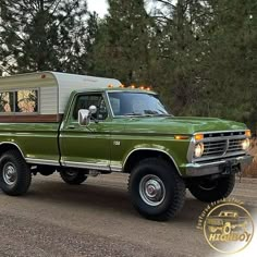 a green truck with a camper on the back parked in front of some trees