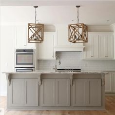 a kitchen with white cabinets and an island that has two pendant lights hanging over it