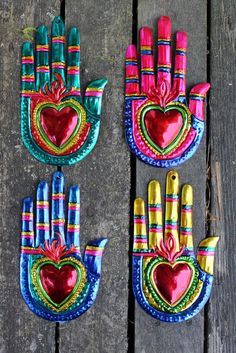 three colorful hand - made items are sitting on a wooden surface, one has a heart and the other has two fingers