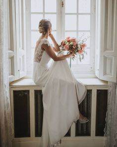 a woman sitting on a window sill holding a bouquet