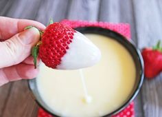 a hand holding a strawberry over a bowl of yogurt