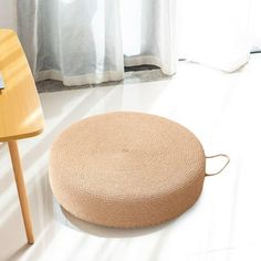 a round rug sitting on the floor next to a wooden table and chair in front of a window