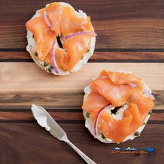 two pieces of bread topped with salmon and onions on top of a wooden cutting board