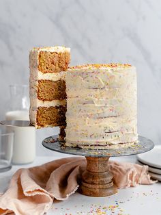 a cake with white frosting and sprinkles sitting on a table next to a glass of milk