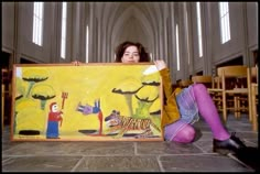 a woman sitting on the floor with a painting in front of her and holding it up