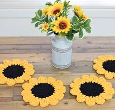 four crocheted sunflower coasters sitting on a table next to a vase with flowers