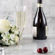 two wine glasses and some flowers on a table next to a bottle of champagne with ice cubes