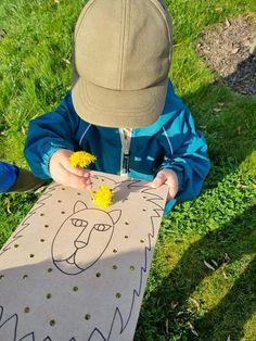 a little boy sitting in the grass with a paper cut out of a lion on it