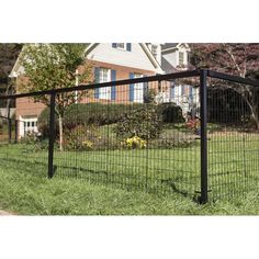 a black wire fence in front of a house with flowers on the lawn behind it