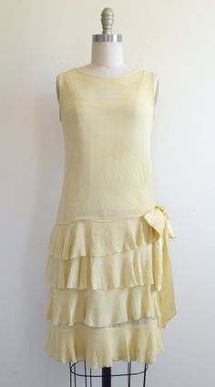 "This antique flapper dress is a delightful pastel yellow and features a silk chiffon overlay, four tiers of frills, and a decorative bow at the left hip. The underlayer is an integral silk slip with a daring bust-line that's just visible through the sheer overlay. Drop-waist. Pullover design (no closure). Excellent, very wearable condition with a few minor cosmetic flaws typical for the age of the garment. Minor color variation throughout due to uneven sun-bleaching, etc (visible in photos). Sm Vintage Drop Waist Dress, Vintage Chiffon Dress, 1920s Flapper Dress For Summer, Vintage Summer Evening Flapper Dress, Fitted Vintage Flapper Dress For Summer, 1920s Style Summer Flapper Dress, Silk Sleeveless Flapper Dress, Vintage Spring Evening Flapper Dress, 1920s Style Silk Summer Dress