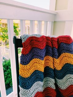 a multicolored crocheted blanket sitting on top of a wooden chair next to a white fence