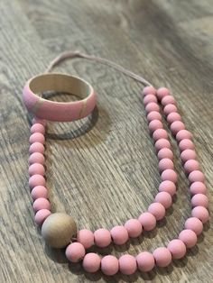 a pink beaded necklace and bracelet on a wooden table with a rubber band around it